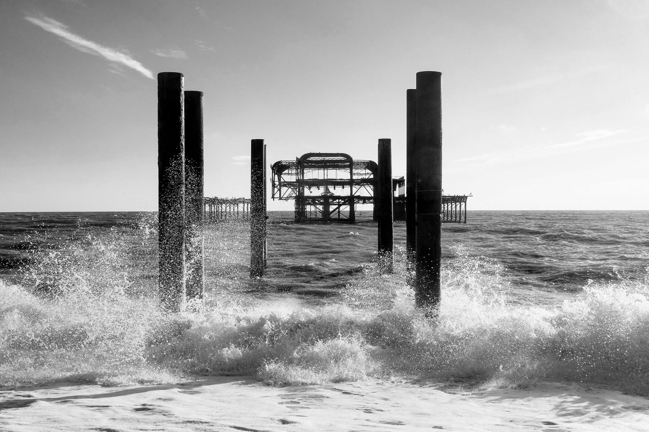 Black and white photo of waves crashing against the pillars of Brighton West Pier