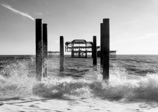 Black and white photo of waves crashing against the pillars of Brighton West Pier