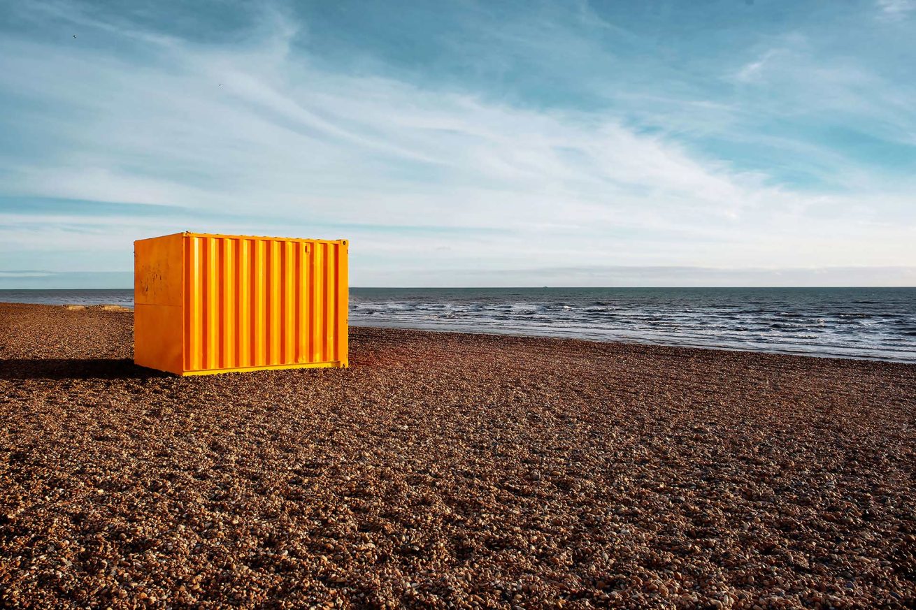 Bright yellow shipping container on Brighton Beach under a blue sky, photographed by Rachel Groom
