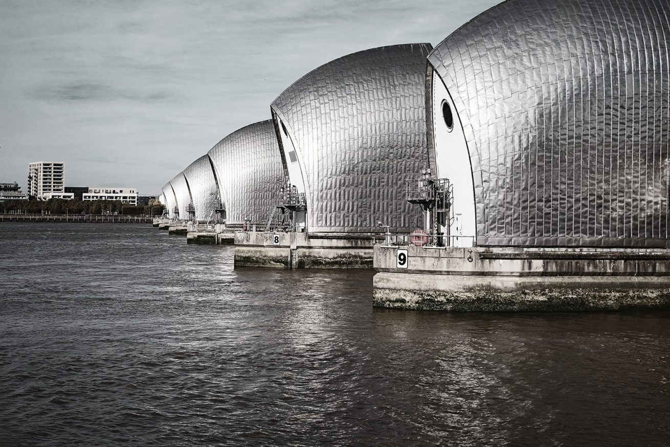 Silver gates of the Thames Barrier in London lined up along the River Thames under a cloudy sky