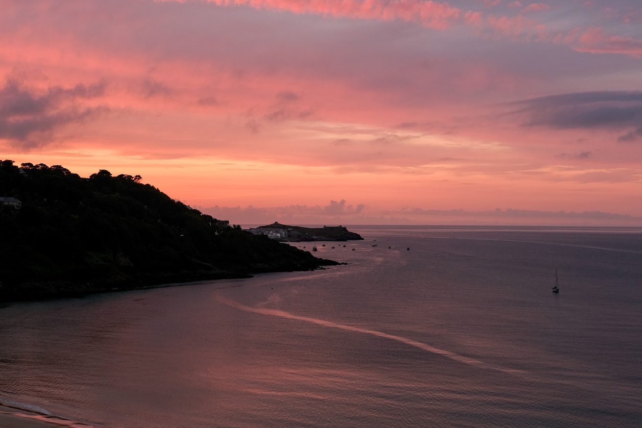 Sunset over St Ives Cornwall with a sailboat on calm water – photo by Rachel Groom Photography
